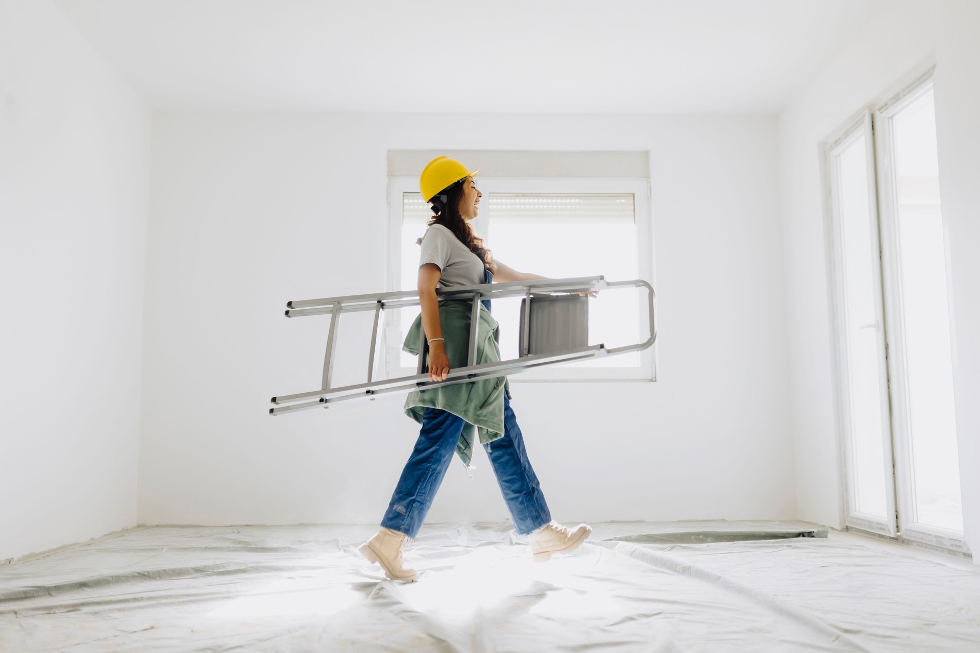 Female worker walking and carrying ladder and paint roller